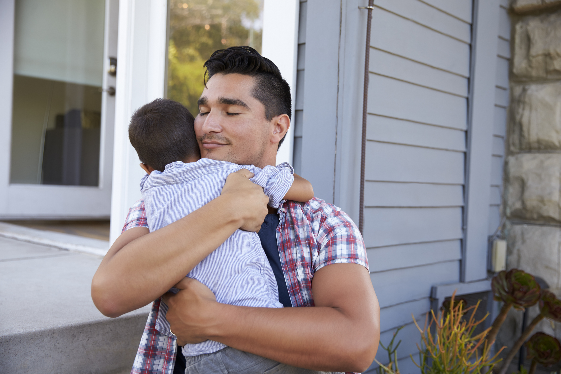 Father hugging his son in front of the house.